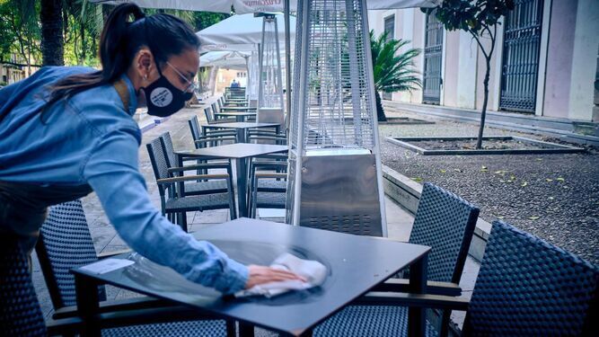 Una camarera desinfecta una mesa de una terraza de la Plaza de Mina.