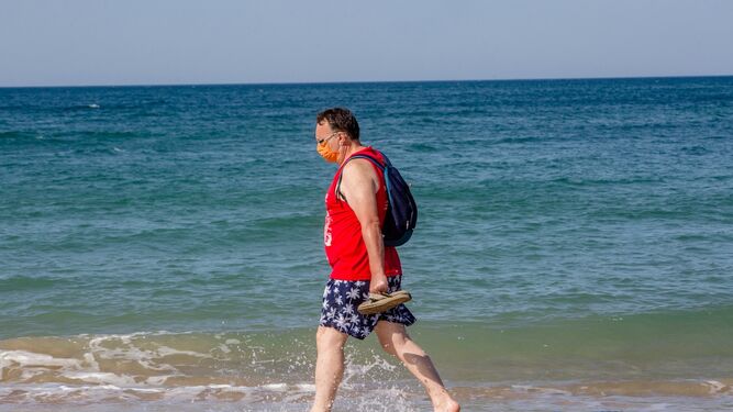 Un hombre pasea por la playa de Cádiz con la mascarilla.