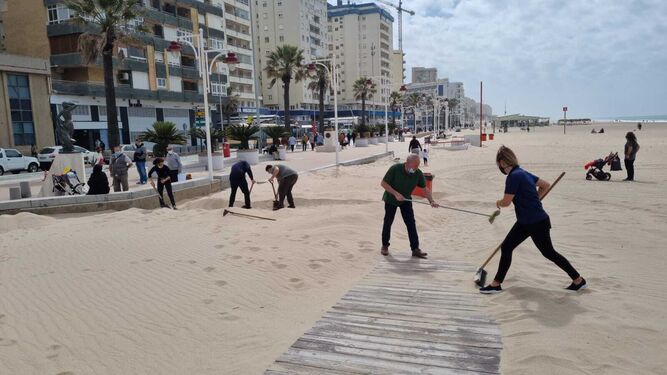 Trabajadores de uno de los chiringuitos mueven la arena para facilitar los accesos.