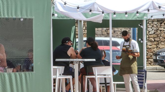 Un camarero sirve a una mesa en un establecimiento de hostelería, este verano en La Barrosa.