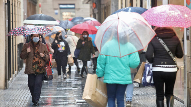 Personas con paraguas por la calle Columela de Cádiz.