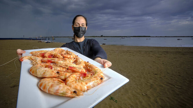 Una camarera de Casa Bigote con un plato de langostinos en la playa de Bajo de Guía, con Doñana al fondo.