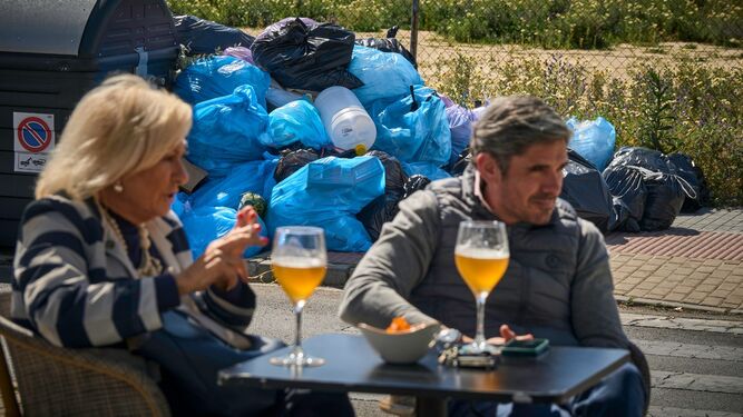 Una pareja tmando unas cervezas en un bar de Vistahermosa delante de un enorme montón de bolsas de basura.