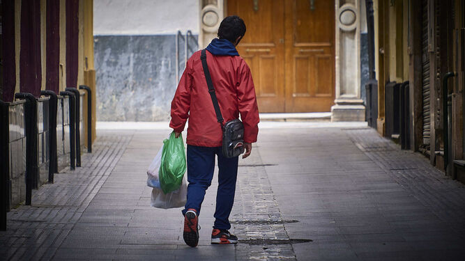 Una persona transita por la calle Santiago tras haber recibido durante el confinamiento bolsas con alimentos en Virgen de Valvanuz.