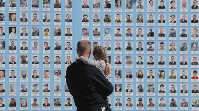 Un ucraniano con una niña en brazos observa el memorial de los caídos en la guerra en Kiev.