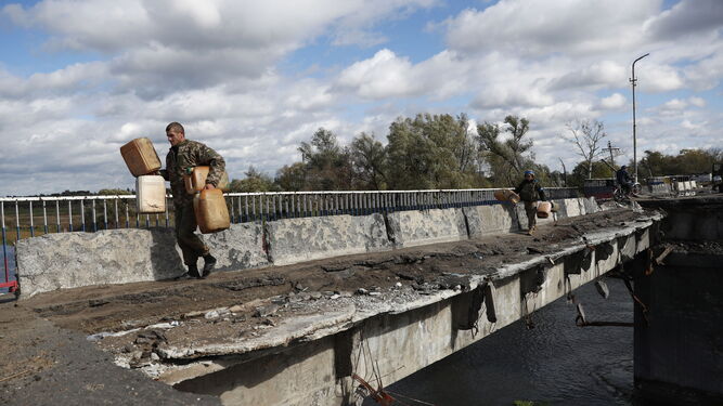 Militares ucranianos portan ayuda a través de un puente destrozado a la recién liberada localidad de Kupiansk.