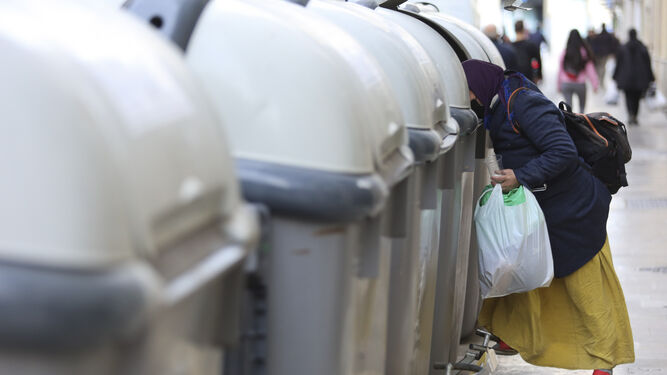 Una mujer rebusca en contenedores de basura.
