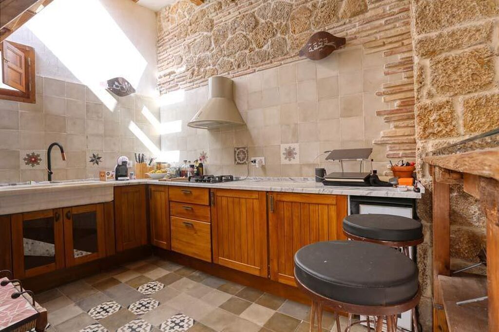 Mobiliario de madera con encimera de m&aacute;rmol de Carrara y pared de piedra ostionera e hidr&aacute;ulico en la cocina.