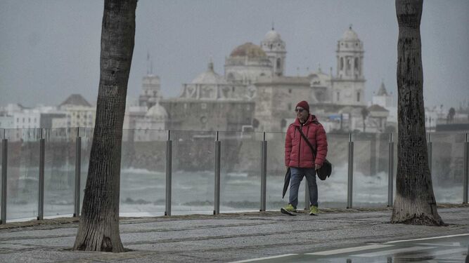 Un hombre camina por Cádiz con el cielo encapotado.