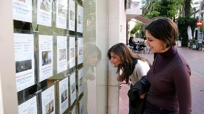 Dos jóvenes miran anuncios en una inmobiliaria