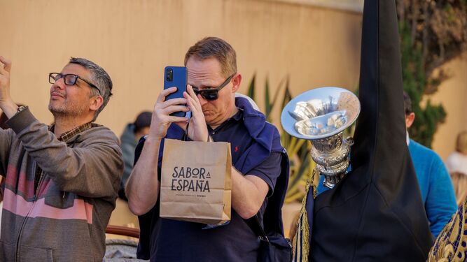 Un turista hace fotos al cortejo de la Hermandad de las Aguas en la Semana Santa de Cádiz 2023