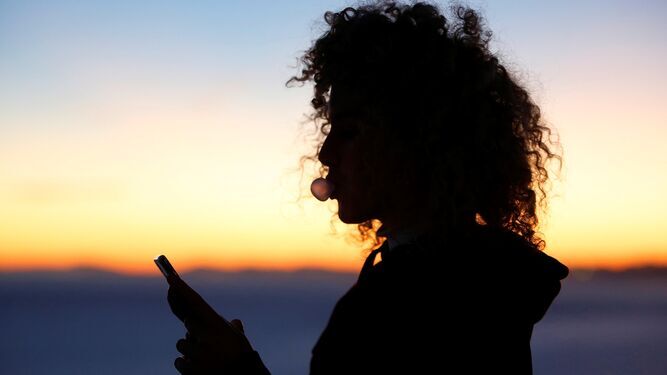 Una joven mirando el móvil durante la puesta de sol