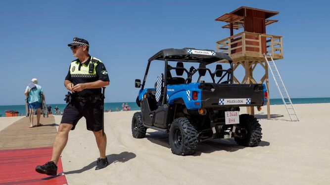 Un agente de la Policía Local esta mañana en la playa Victoria junto a un vehículo de patrulla.