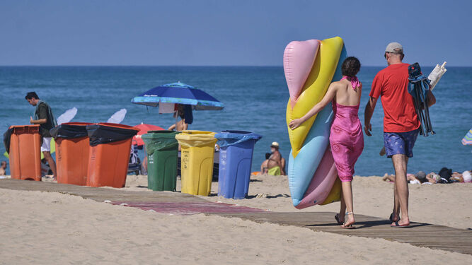 Usuarios de la playa  Victoria con un hinchable pasan junto a las papeleras dispuestas en la arena.