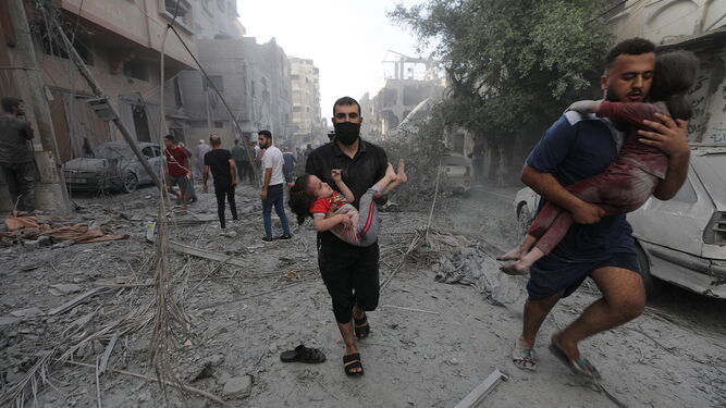 Dos hombres palestinos trasladan en brazons a niños heridos tras los ataques aéreos israelíes en el norte de Gaza.