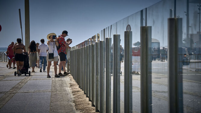 Varias personas caminan por el Paseo Marítimo de Cádiz en un día soleado y de calor