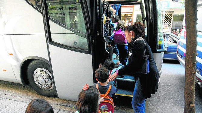 Una monitora ayuda a subir a alumnos en un autobús escolar.